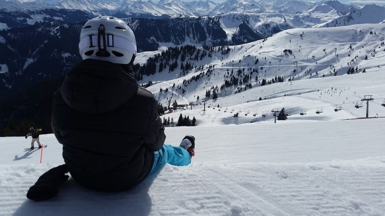 Austria, góry, na śniegu siedzi narciarz w kombinezonie i kasku.